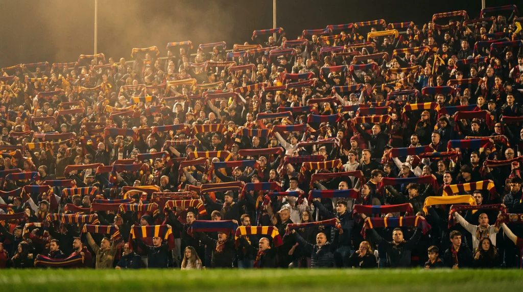 Tribuna gremita di tifosi in uno stadio italiano durante una partita di Serie A in notturna
